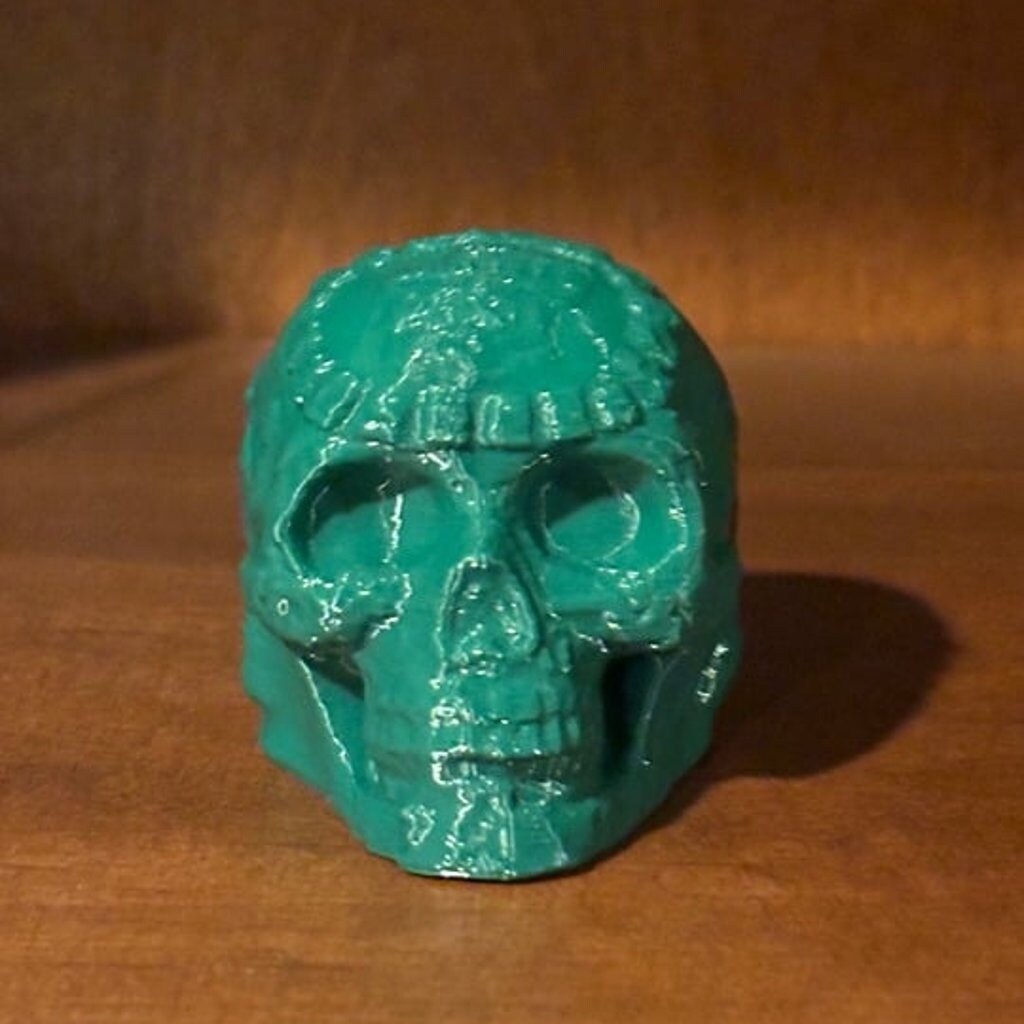 An intricately crafted Mayan death whistle in a rich forest green color, featuring an Aztec skull design with detailed carvings. The whistle is displayed against a white background, highlighting its unique and striking appearance.