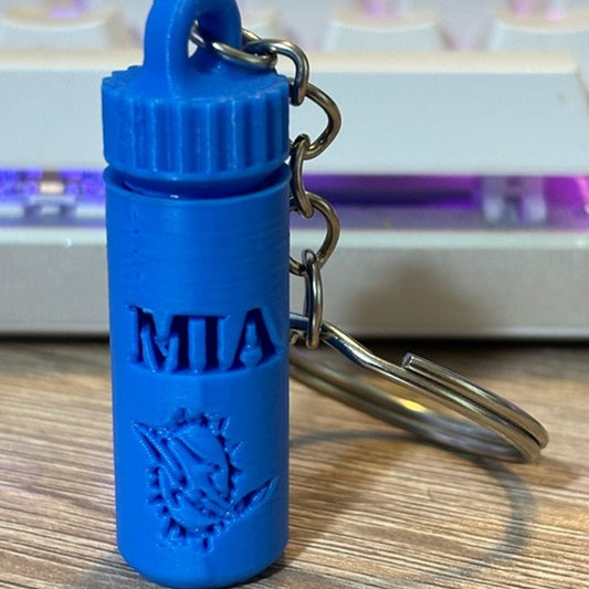 A clear pill bottle keychain filled with small pink flamingo shapes, labeled with &quot;MIA Miami&quot; in black text, shown against a white background, made in the USA and representing a Miami-themed party accessory.