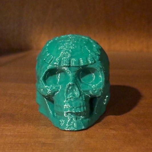 An intricately crafted Mayan death whistle in a rich forest green color, featuring an Aztec skull design with detailed carvings. The whistle is displayed against a white background, highlighting its unique and striking appearance.